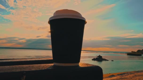日落时在路堤上的长椅上的纸杯里喝咖啡 日落时的柔和日光 日落时分在海滨长廊附近的杯子里喝咖啡 — 图库视频影像