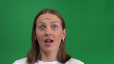 Mutluluktaki güzel kız ellerini yeşil bir arka planda tutarak yüzünü kapatıyor. Genç kadın çok mutlu, yeşil ekranda izole edilmiş, krom ada. Kadın başarı için gülümsüyor ve çığlık atıyor..