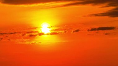 Time lapse bright orange sunset sun sets behind the clouds. The end of the day, the sun goes below the horizon. Big red hot sun in warm air distortion above the horizon.