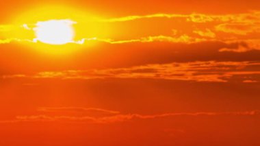 Time lapse bright orange sunset sun sets behind the clouds. The end of the day, the sun goes below the horizon. Big red hot sun in warm air distortion above the horizon.