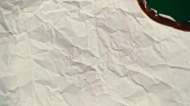 White paper burns from above on a green background copy space. The sheet of paper burns and reveals a green background for pasting.