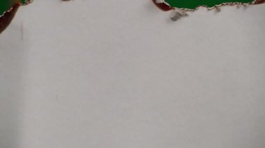 White paper burns from above on a green background copy space. The sheet of paper burns and reveals a green background for pasting.