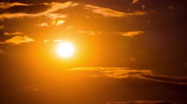 Time lapse bright orange sunset sun sets behind the clouds. The end of the day, the sun goes below the horizon. Big red hot sun in warm air distortion above the horizon.