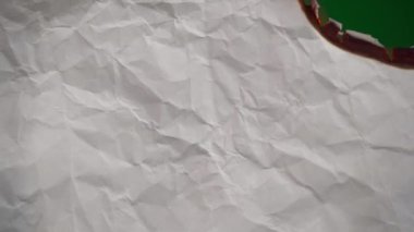 White paper burns from above on a green background copy space. The sheet of paper burns and reveals a green background for pasting.