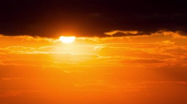 Time lapse bright orange sunset sun sets behind the clouds. The end of the day, the sun goes below the horizon. Big red hot sun in warm air distortion above the horizon.