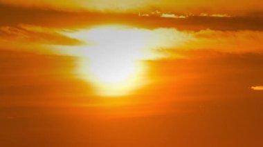 Time lapse bright orange sunset sun sets behind the clouds. The end of the day, the sun goes below the horizon. Big red hot sun in warm air distortion above the horizon.