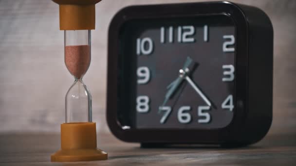 Sanduhr Nahaufnahme Ergießt Sich Vor Dem Hintergrund Gewöhnliche Mechanische Uhr — Stockvideo