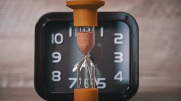 Sanduhr Nahaufnahme Ergießt Sich Vor Dem Hintergrund Gewöhnliche Mechanische Uhr — Stockvideo