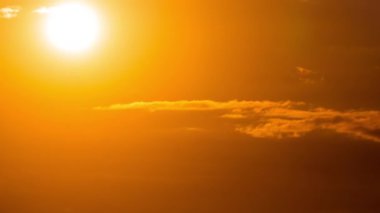 Parlak turuncu gün batımı bulutların arkasında batıyor. Günün sonunda, güneş ufkun altına batar. Ufkun yukarısındaki sıcak hava bükümünde büyük kırmızı güneş..