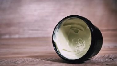 Masanın üzerinde bir kavanoz krema var ve bir kadının parmağı alıyor. Kadın yüzünü ve vücudunu nemlendiriyor. Kadınların güzelliği ve cilt bakımı. Güzel kadın tırnakları.