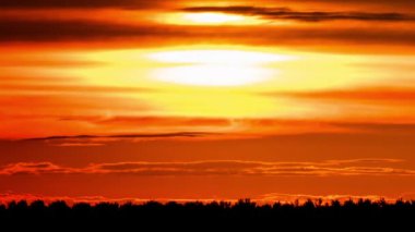 Parlak turuncu gün batımı bulutların arkasında batıyor. Günün sonunda, güneş ufkun altına batar. Ufkun yukarısındaki sıcak hava bükümünde büyük kırmızı güneş..