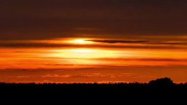 Parlak turuncu gün batımı bulutların arkasında batıyor. Günün sonunda, güneş ufkun altına batar. Ufkun yukarısındaki sıcak hava bükümünde büyük kırmızı güneş..