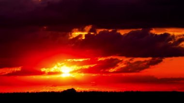 Time lapse bright orange sunset sun sets behind the clouds. The end of the day, the sun goes below the horizon. Big red hot sun in warm air distortion above the horizon.