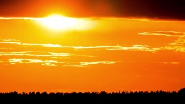 Parlak turuncu gün batımı bulutların arkasında batıyor. Günün sonunda, güneş ufkun altına batar. Ufkun yukarısındaki sıcak hava bükümünde büyük kırmızı güneş..