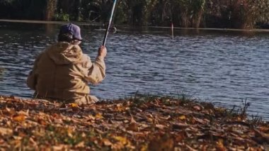 Yaşlı kadın sonbaharda bir gölette balık tutuyor. Açık havada balık yakalayan bir oltayla yaşayan bir insanın geri kalanı. Yaşlı elbiseli büyükanne oltayla balık tutuyor..