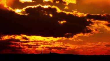 Time lapse bright orange sunset sun sets behind the clouds. The end of the day, the sun goes below the horizon. Big red hot sun in warm air distortion above the horizon.