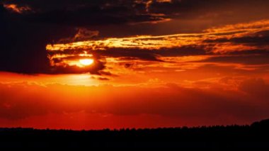 Time lapse bright orange sunset sun sets behind the clouds. The end of the day, the sun goes below the horizon. Big red hot sun in warm air distortion above the horizon.