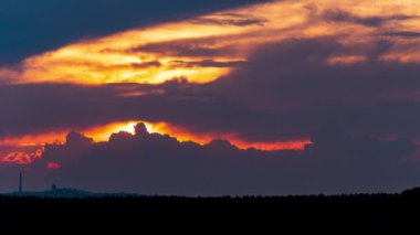 Parlak turuncu gün batımı bulutların arkasında batıyor. Günün sonunda, güneş ufkun altına batar. Ufkun yukarısındaki sıcak hava bükümünde büyük kırmızı güneş..