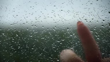 Kız bardağa yakın plan yağmur damlalarıyla kalp çiziyor. Yağmurlu hava ve üzüntü. Yağmurlu bir gün ve bulutlu bir hava. Bulutlu gökyüzü, gri hava.