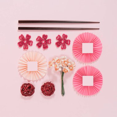 Neatly arranged Chinese New Year homemade decorations and props. Minimal flat lay aesthetic on pastel pink background.