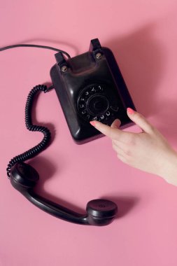 Kadın eli ve klasik telefonuyla yaratıcı retro tarzı görsel. Devam eden çağrı konsepti. Pastel pembe arka planda düz kompozisyon.