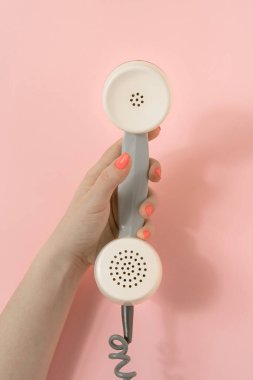 Eski bir sahne, kadın el kaydırmalı retro telefon alıcısı. Pastel pembe arka planda minimum kompozisyon. Üst görünüm.