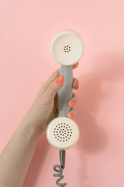 Vintage scene with female hand scrolling retro phone receiver. Minimal composition on pastel pink background. Top view.