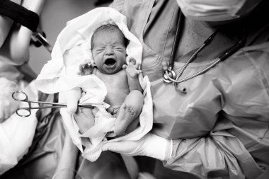 Doktor çocuk doktoru doğum odasında yeni doğmuş bir bebeği kollarına aldı.