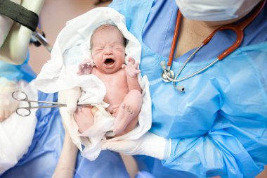 Doktor çocuk doktoru doğum odasında yeni doğmuş bir bebeği kollarına aldı.