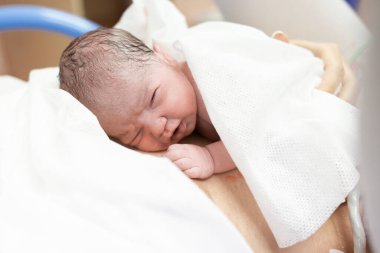 Yeni doğan bebek, doğum hastanesindeki doğum odasında annesinin üzerine yatar.