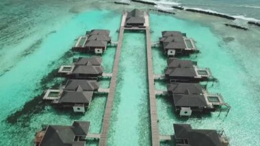 Tropik Maldivler 'de kumlu kumlu ve mavi lagünü olan egzotik turkuaz cenneti gösteren hava aracı videosu. Su villası bungalovlarının havadan görünüşü. Yüksek kalite 4K görüntü. Maldivler 'deki lüks tatil beldesi.