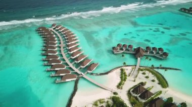 Tropik Maldivler 'de kumlu kumlu ve mavi lagünü olan egzotik turkuaz cenneti gösteren hava aracı videosu. Su villası bungalovlarının havadan görünüşü. Yüksek kalite 4K görüntü. Maldivler 'deki lüks tatil beldesi.