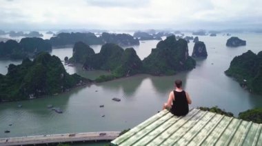 Çatıda dikilmiş Vietnam 'daki Mystical Ha Long Körfezi' ne bakan bir adamın hava görüntüleri. Halong Körfezi 'nde ünlü bir yer. Vietnam 'daki en iyi seyahat turizmi. Yüksek kalite 4k görüntü.