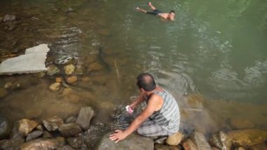 Pohnpei, Micronesia - July 23, 22: Dad with a son takes a bath in a lake full of freshwater large eels. Small village inside a jungle. High quality 4k footage