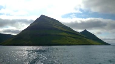 Ferry arriving to Kalsoy Island. Amazing Faroese nature. Faroese Cliffs and mountains. Green hills and beautiful rocky mountains. View to a Kalsoy Island. Sunny day in summer. 4k footage