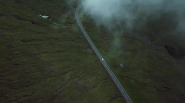Aerial view of an amazing mist Faroese nature with a car driving on a road. Flying above the clouds. High quality 4k footage