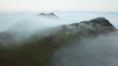 Aerial view of an amazing mist Faroese nature, foggy green hills and beautiful rocky cliffs and mountains. Flying above the clouds. High quality 4k footage