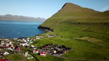 Aerial view of Gjogv village and Tyril mountain in Faroe Islands. Sunny day in summer. Amazing nature in Faroe Islands. Eysturoy Island. Birds on the footage. Faroese canyon.