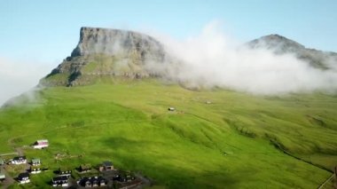 Aerial view of a foggy Arnafjall, highest mountain in Vagar Island, Faroe Islands. Small village Gasadalur with a Hvannadalur valley. Sunny day in summer. High quality 4k footage.