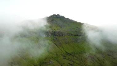 Aerial view of an amazing mist Faroese nature, foggy green hills and beautiful rocky cliffs and mountains. Flying above the clouds. High quality 4k footage