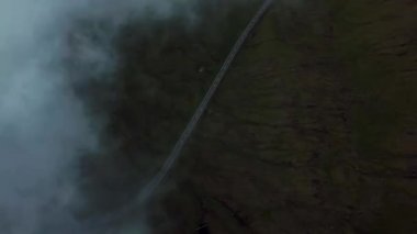 Aerial view of an amazing mist Faroese nature with a car driving on a road. Flying above the clouds. High quality 4k footage