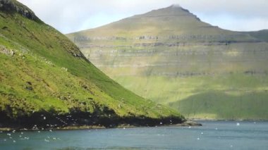 Ferry arriving to Kalsoy Island. Amazing Faroese nature with a lot of sea birds. Faroese Cliffs and mountains. Green hills and beautiful rocky mountains. View to a Kalsoy Island. Sunny day in summer.