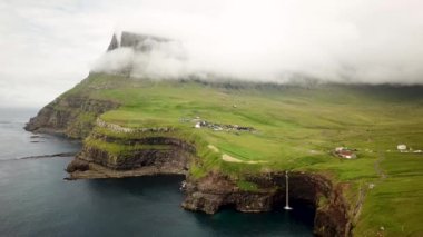 Aerial view of Mulafossur waterfall, Faroe Islands. Small village Gasadalur with a Hvannadalur valley and Arnafjall mountain hidden in a fog. Sunny day in summer. High quality 4k footage.