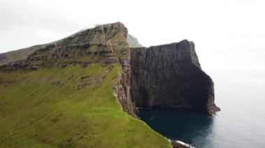 Faroe Adaları 'ndaki Drangarnir ve Tindholmur yakınlarındaki büyük uçurumların insansız hava aracı görüntüsü. Muhteşem Faroe doğası, yeşil tepeler ve güzel kayalıklar ve dağlar. Yazın güneşli bir gün. Kaliteli 4k görüntü.