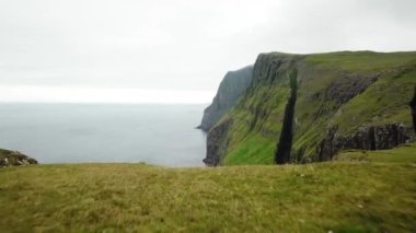 Dunnesdrangar, Faroe Adaları 'na bakan bir kızın 4K hava aracı görüntüsü. İnanılmaz doğa, Faroe Adaları 'ndaki büyük kayalıklar ve dağlar. Vagar Adası. Bir sürü uçan deniz kuşu. Yazın güneşli bir gün.