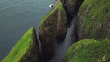 Dunnesdrangar, Faroe Adaları 'na bakan bir adamın 4K hava aracı görüntüsü. İnanılmaz doğa, Faroe Adaları 'ndaki büyük kayalıklar ve dağlar. Vagar Adası. Bir sürü uçan deniz kuşu. Yazın güneşli bir gün.