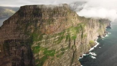Faroe Adaları 'ndaki Kalsoy adasının insansız hava aracı görüntüsü. Muhteşem Faroe doğası, yeşil tepeler ve güzel kayalıklar ve dağlar. Kallur deniz feneri. Yazın güneşli bir gün. Faroe 'da film. 4k görüntü