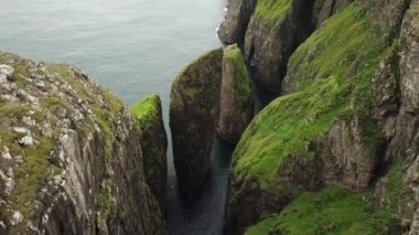 Dunnesdrangar, Faroe Adaları 'na bakan bir adamın 4K hava aracı görüntüsü. İnanılmaz doğa, Faroe Adaları 'ndaki büyük kayalıklar ve dağlar. Vagar Adası. Bir sürü uçan deniz kuşu. Yazın güneşli bir gün.