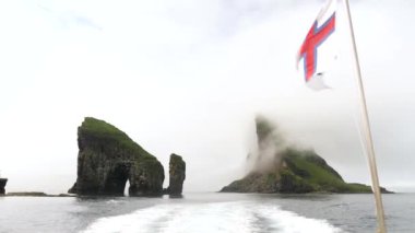 Faroe Adaları 'nda ulusal bayrak taşıyan Drangarnir ve Tindholmur' un tekne manzarası. Kaya oluşumları Drangarnir Deniz Yığını ve Atlas Okyanusu 'ndaki Tindholmur Adası. Yüksek kalite 4k görüntü.