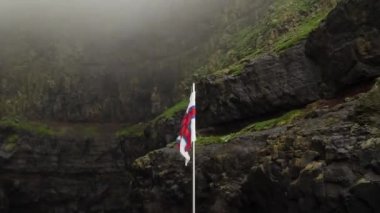 Faroe Adaları 'ndaki Mykines Adası' nda gizlenmiş yüksek uçurum koyundan ayrılan bir tekne. Faroe bayrağı. Yüksek kalite 4k görüntü.